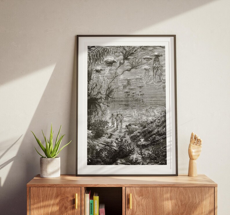 May include: Black and white framed print of an underwater scene with figures, jellyfish, and aquatic plants. The detailed illustration depicts a vintage, fantastical environment with a sense of depth and mystery. The artwork is displayed on a wooden cabinet.