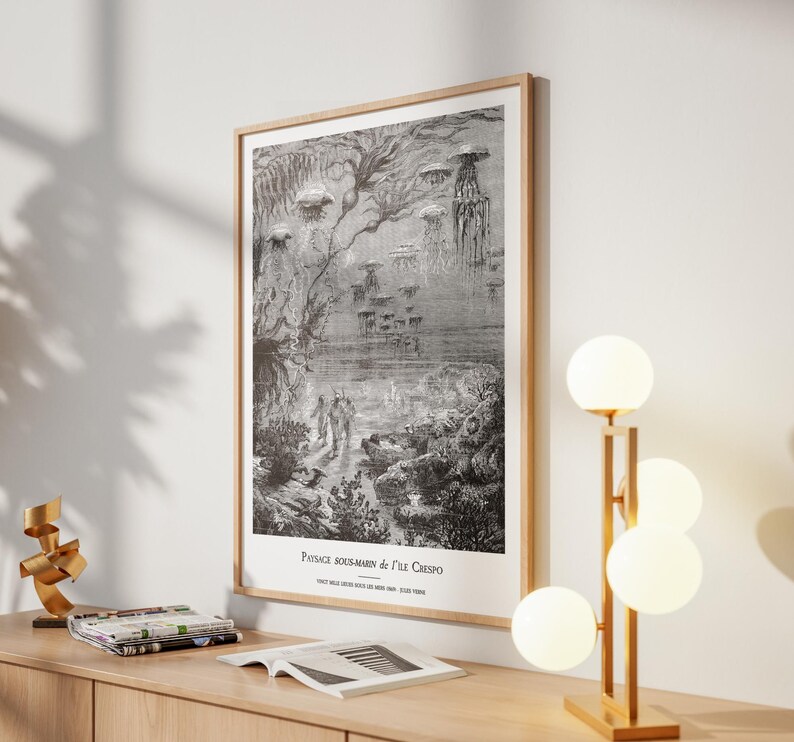 May include: A framed black and white illustration depicting an underwater scene with jellyfish and figures. The artwork, titled "Paysage Sous-Marin de l'Ile Crespo," is displayed on a wooden table with a modern lamp and decorative items.