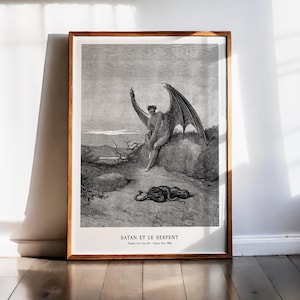 Op de afbeelding: Een ingelijste zwart-wit print met een gedetailleerde illustratie van een gevleugelde figuur zittend op een rots, met een slang eronder. De print zit in een houten lijst en bevat de tekst "SATAN ET LE SERPENT".