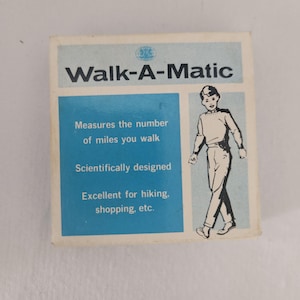 May include: A vintage box for a "Walk-A-Matic" pedometer. The box is white and light blue, with text that reads "Measures the number of miles you walk." A black and white illustration of a person walking is on the right side.