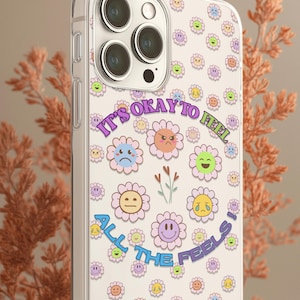 May include: Clear phone case with a repeating pattern of smiling flower faces in various colors. The case has the text "It's okay to feel all the feels!" in a curved design.
