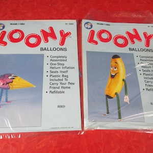 Op de afbeelding: Twee verzegelde verpakkingen van "Loony Balloons". Eén heeft een vogelvormige ballon met een gele snavel en een paarse kop. De andere is een banaanvormige ballon met het label "Bananaman". Beide zijn ontworpen voor heliuminflatie.