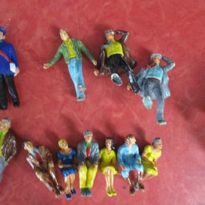 May include: A selection of small, painted figurines depicting people in various poses. The figures include a police officer and people in casual attire. The figurines are likely intended for use in a model railway or diorama, and are brightly coloured.
