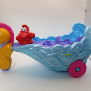 May include: A Little People toy featuring a yellow seahorse pulling a blue and purple boat with a red crab figure. The boat has a pink wheel and the words "Little People" are printed on the side.