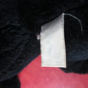 Op de afbeelding: Close-up van een zwart pluche speelgoed met een wit label eraan. Het label heeft tekst die moeilijk te lezen is. Het pluche speelgoed lijkt gemaakt te zijn van een zacht, fuzzy materiaal.