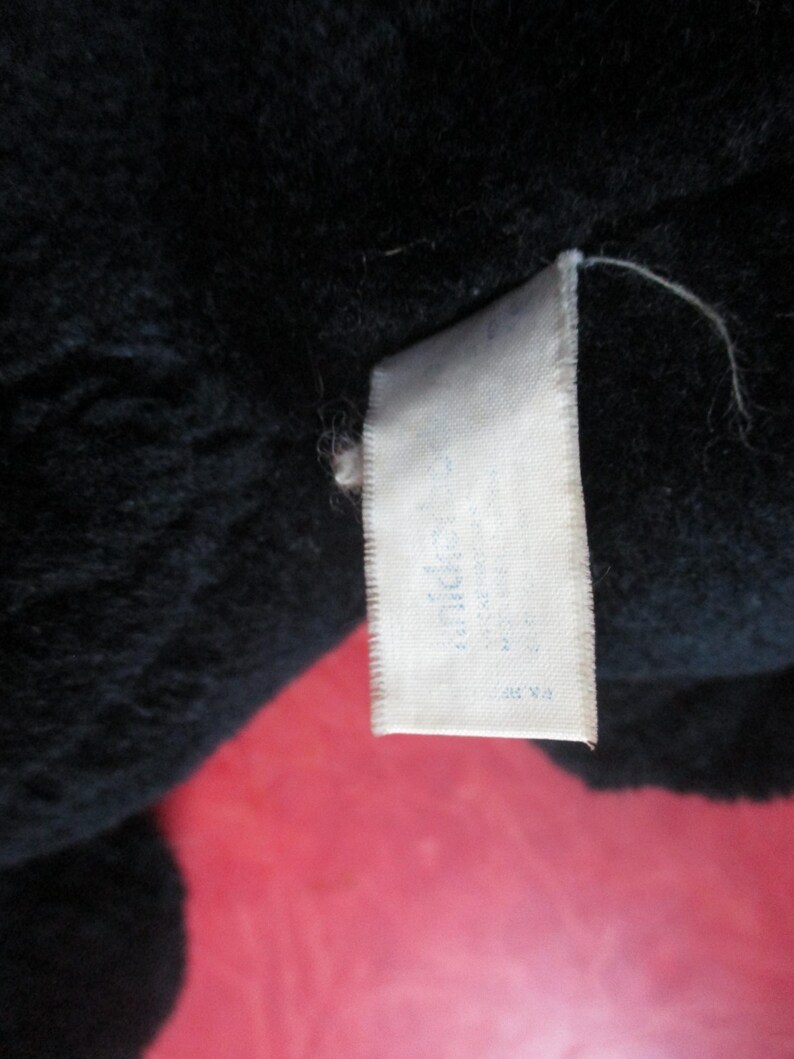 Op de afbeelding: Close-up van een zwart pluche speelgoed met een wit label eraan. Het label heeft tekst die moeilijk te lezen is. Het pluche speelgoed lijkt gemaakt te zijn van een zacht, fuzzy materiaal.