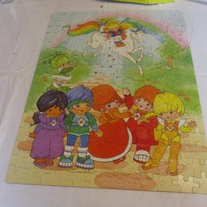 Könnte beinhalten: Fertig gepuzzeltes Puzzle mit einer farbenfrohen Cartoon-Illustration. Das Bild zeigt einen Regenbogen, ein Einhorn und mehrere Figuren in verschiedenen Outfits. Das Puzzle liegt auf einer hellen Oberfläche.