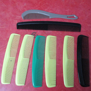 May include: A collection of hair combs in various colors and styles. The combs include a gray comb with a handle, a black comb, and several yellow and green combs. The combs are arranged on a red surface.