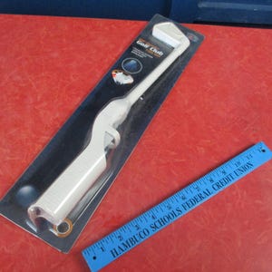 Peut inclure: Un briquet blanc en forme de club de golf dans son emballage d'origine, avec les mots "Golf Club" visibles. Une règle bleue avec du texte blanc est également présente. Les articles sont sur une surface rouge.