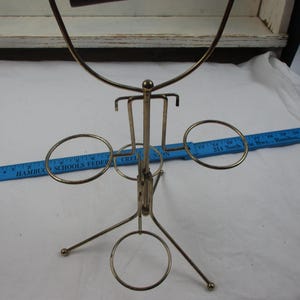 May include: A vintage metal serving stand with a dark brown wooden handle. The stand has a gold-colored finish and features several circular holders and a central support structure. The base has three legs.