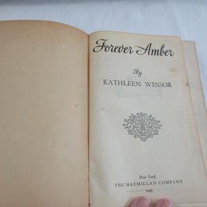 Può includere: Libro aperto con il titolo "Forever Amber" di Kathleen Winsor. Le pagine sono color crema, mostrando segni di invecchiamento. La copertina mostra il nome dell'editore, The Macmillan Company, e l'anno 1945.
