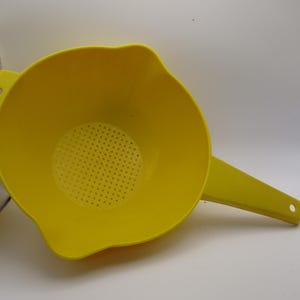 Peut inclure: Une passoire en plastique jaune vif dotée d'un bol rond avec une base perforée pour égoutter les liquides. L'ustensile de cuisine comprend une longue poignée plate d'un côté et une petite languette avec un trou circulaire pour suspendre.