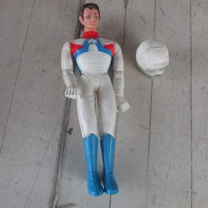 May include: A white and blue action figure with a red, white, and blue chest piece. The figure has a helmet that is white with a blue visor.