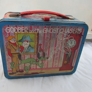 May include: Vintage metal lunchbox featuring the cartoon "Goober and the Ghost Chasers." The lunchbox has a blue frame with a red handle. The front panel displays cartoon characters, a portrait, and a grandfather clock.