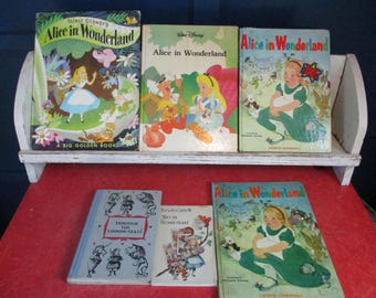 May include: A collection of vintage children's books featuring the title "Alice in Wonderland." The books are displayed on a white shelf and a red surface. The covers showcase colorful illustrations of Alice and other characters from the story.