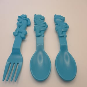May include: Three light blue plastic utensils: a fork and two spoons. Each utensil features a Winnie the Pooh figure at the top of the handle. The fork has four tines, while the spoons have oval bowls. The set is designed for children.