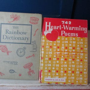 Puede incluir: Dos libros antiguos. El primer libro se titula "The Rainbow Dictionary" con ilustraciones rojas y azules. El segundo libro se titula "742 Heart-Warming Poems" con una portada roja y un fondo con estampado amarillo.