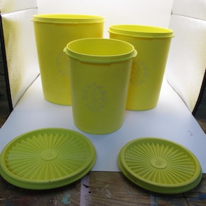 Può includere: Tre contenitori in plastica giallo brillante con coperchi circolari abbinati. Ogni contenitore presenta un sottile motivo floreale di colore chiaro sulla parte anteriore. I recipienti sono cilindrici con finitura liscia e bordo semplice.