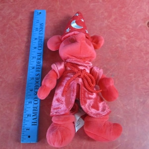 May include: A plush red wizard doll with a pointed hat adorned with a crescent moon and stars. The doll is wearing a red robe and boots. A blue ruler, approximately 8 inches long, is next to the doll.