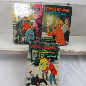 May include: Three vintage Trixie Belden hardcover books featuring illustrated covers. Titles include Trixie Belden and the Mysterious Code and Trixie Belden and the Black Jacket Mystery, with colorful depictions of characters in various mystery scenes.