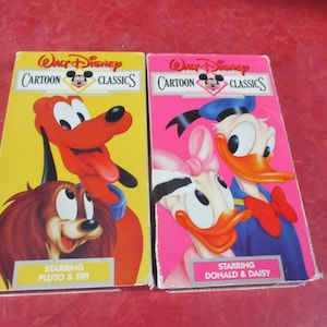 Puede incluir: Dos cintas VHS clásicas de dibujos animados de Walt Disney. Una presenta a Pluto y Fifi sobre un fondo amarillo, la otra a Donald y Daisy Duck sobre un fondo rosa. Las cintas tienen el logotipo de Disney.