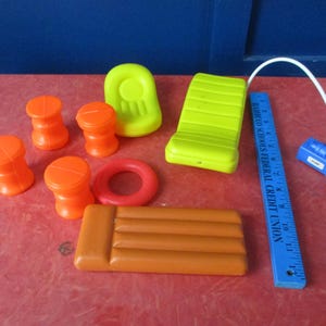 以下が含まれることがあります： カラフルなプラスチック製のプールとビーチのおもちゃのコレクション。オレンジ色のスツール、赤い浮き輪、黄色のラウンジチェア、茶色のいかだ、青い定規、黄色の椅子、青い空気ポンプが含まれています。