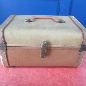 Puede incluir: Maleta vintage marrón y beige con asa color melocotón y cierre metálico. La maleta rectangular tiene esquinas redondeadas y bordes reforzados. El exterior muestra signos de desgaste, lo que añade encanto antiguo.