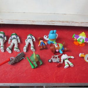 May include: A selection of Toy Story character figures, including Buzz Lightyear, Woody, Mr. Potato Head, and others. The toys are displayed on a red surface, with a white shelf in the background. Various accessories are also present.
