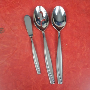 Könnte beinhalten: Ein Set aus drei Servierutensilien aus Edelstahl: ein Buttermesser, ein Schöpflöffel und ein Servierlöffel. Die Utensilien haben ein schlankes, modernes Design mit länglichen Griffen. Der Hintergrund ist einfarbig rot.