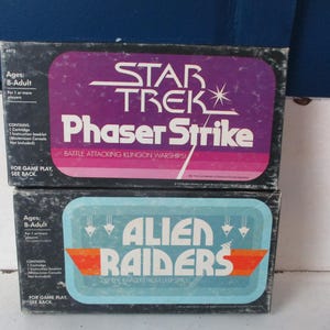 May include: Two vintage video game boxes. The top box features a purple label with "STAR TREK Phaser Strike" text. The bottom box has a blue label with "ALIEN RAIDERS" text. Both boxes are for ages 8-adult.