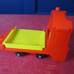 Puede incluir: Un camión de juguete de color naranja brillante y amarillo con una plataforma. El camión tiene una plataforma amarilla y una cabina y carrocería naranja. El juguete tiene dos ruedas negras y es de plástico.