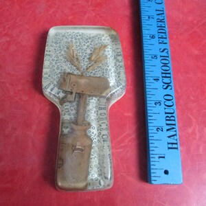 May include: A clear resin spoon rest with embedded wheat stalks and a rustic-style design featuring a hammer and a milk jug. The spoon rest is approximately 6 inches long. A blue ruler is next to the spoon rest.