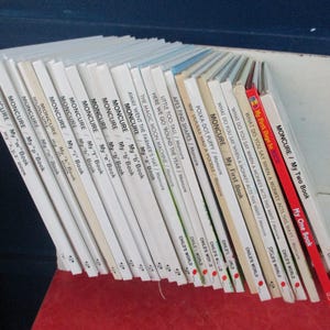 Puede incluir: Una colección de libros infantiles antiguos, apoyados contra una superficie blanca. Los libros tienen lomos blancos con títulos como "My First Book" y "My Two Book" en texto rojo y negro. Los libros son de la serie "Child's World".