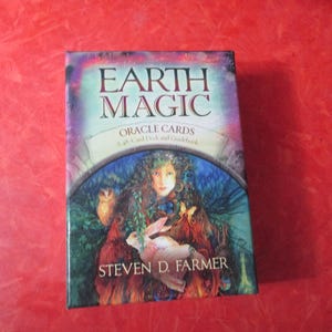 May include: A deck of Earth Magic Oracle Cards with a 48-card deck and guidebook. The box features the title "Earth Magic" in large letters, with an illustration of a woman with an owl and a rabbit. The author's name, Steven D. Farmer, is also visible.