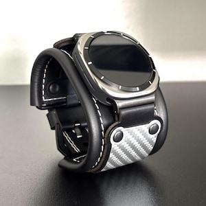May include: A black leather watch band with a silver watch face. The band has white stitching and a carbon fiber accent. The watch face is round with a black screen. The band is designed to fit a smartwatch.