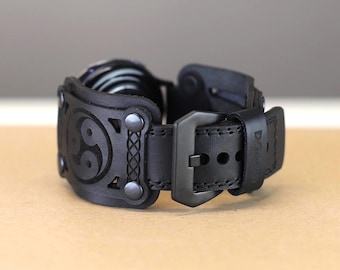 May include: Black leather watch band with a black buckle and a decorative design featuring a yin yang symbol.