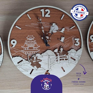 Può includere: Un orologio rotondo in legno con un design di ispirazione giapponese. Il quadrante dell'orologio presenta uno sfondo marrone, un anello esterno bianco e numeri. Il design include una pagoda, figure e uccelli. L'orologio è etichettato "Fabriqué en France Normandie".