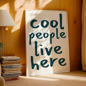 May include: A white framed poster with the text "cool people live here" in teal blue lettering.