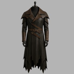 Può includere: Un lungo cappotto in pelle marrone scuro con colletto, spalle e polsini marroni a contrasto. Il cappotto presenta una cintura in vita e un orlo a zig-zag unico. Il cappotto è esposto su un manichino nero.