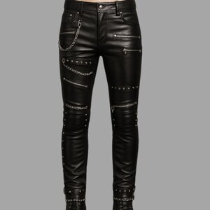 May include: Black leather pants with multiple zippers, silver chain detailing, and studded accents. The pants have a classic five-pocket design and a slim fit. The zippers and studs add a punk rock or biker aesthetic.