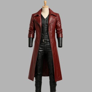 Peut inclure: Un long manteau en cuir rouge bordeaux avec des manches en cuir noir, une chemise et un pantalon noirs. Le manteau a un col cranté, une ceinture et une coupe longue. L'ensemble est présenté sur un mannequin.