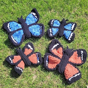 May include: Four crocheted butterfly decorations in blue, orange, and black. The butterflies are made with yarn and have a fluffy texture.