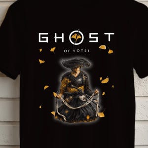Może przedstawiać: Czarna koszulka z białym napisem "GHOST of YOTEL" i ilustracją samuraja. Projekt przedstawia samuraja w czarnym i złotym stroju. Koszulka jest prezentowana na drewnianym wieszaku na tle ceglanej ściany.