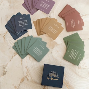 May include: A set of affirmation cards with a blue box that says "Joy Affirmations". The cards are in various colors, including green, brown, and purple. Each card has a different affirmation printed on it in white text.