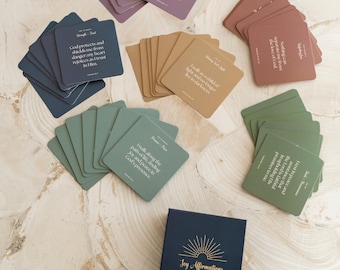 May include: A set of affirmation cards with a blue box that says "Joy Affirmations". The cards are in various colors, including green, brown, and purple. Each card has a different affirmation printed on it in white text.