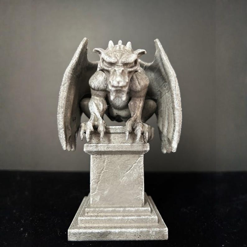 K&ouml;nnte beinhalten: Eine graue Gargoyle-Statue mit detaillierten Fl&uuml;geln, Krallen und einem grimmigen Gesichtsausdruck. Die Statue thront auf einem quadratischen Sockel und zeigt einen gotischen Architekturstil. Die Skulptur besteht aus einem stein&auml;hnlichen Material.