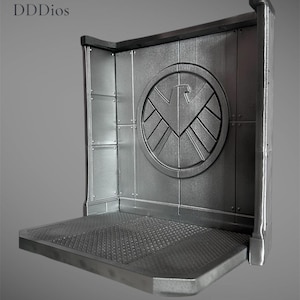 May include: A silver-colored display stand with a textured platform and a wall featuring a circular emblem with a stylized bird design. The stand has a corner design and is made of metal. The text "DDDios" is in the upper left corner.