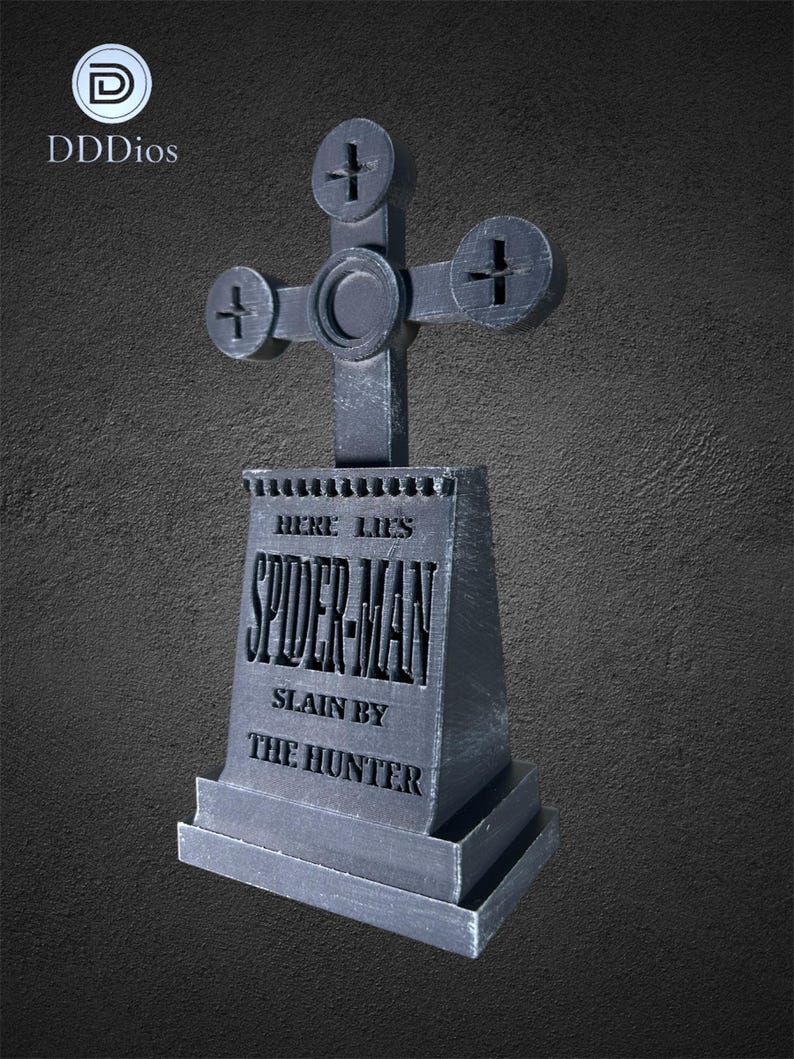 May include: A gray tombstone with a cross-shaped top. The tombstone reads "HERE LIES SPIDER-MAN SLAIN BY THE HUNTER." The design is a unique, stylized tribute to the comic book character.