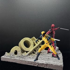 Può includere: Action figure di Wolverine in giallo e blu e Deadpool in rosso, posizionate su una base diorama. La base presenta una struttura in rovina con le lettere "O" e "L". Entrambe le figure impugnano spade.