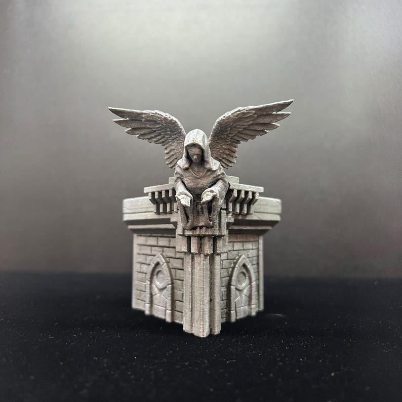 May include: A 3D printed miniature of a stone tower with a hooded angel figure perched on top. The tower has a square base and a pointed roof. The angel has wings spread out and is looking down.